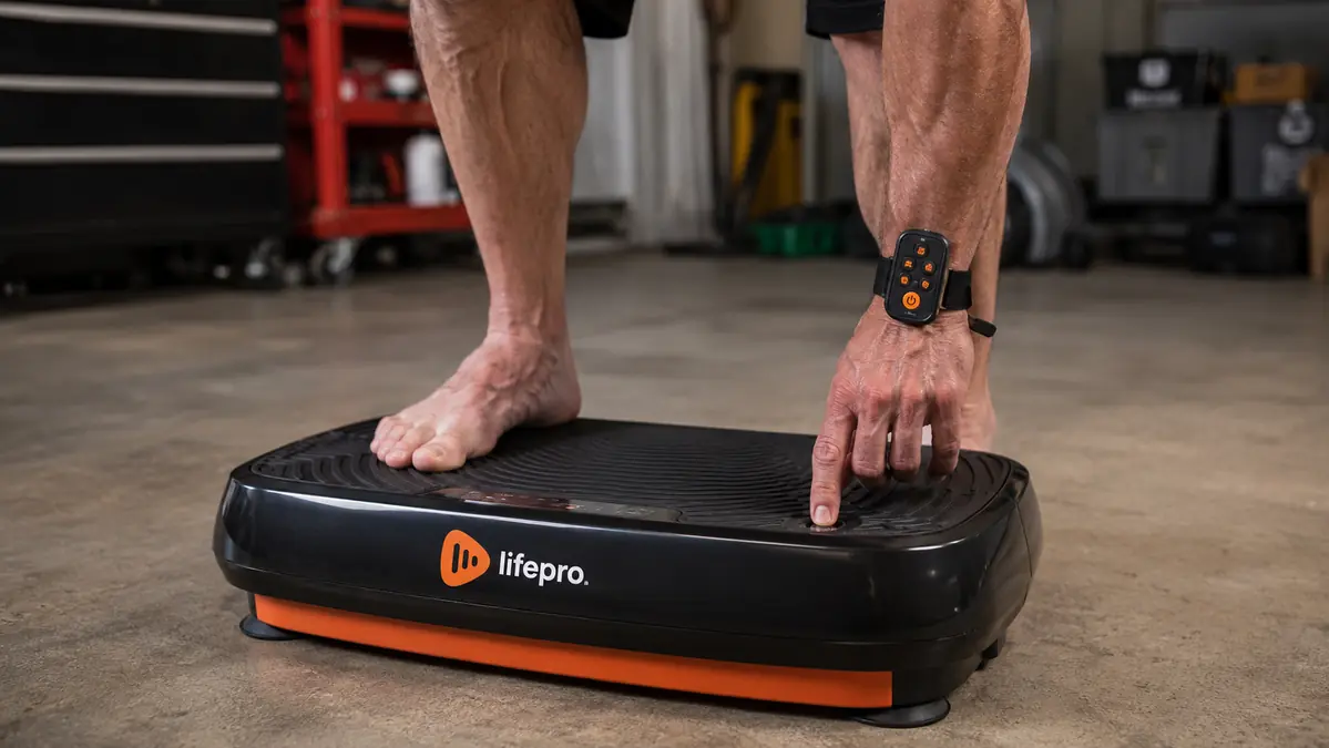 Close-up of bare feet on the textured platform of a vibration plate with the wrist remote visible